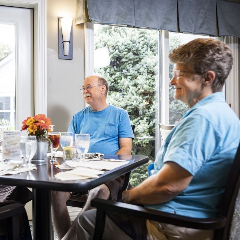 A senior couple shares a meal in a sunny dining setting at Willow Brook in Delaware, Ohio, used as the mobile header for the Lifestyle page.