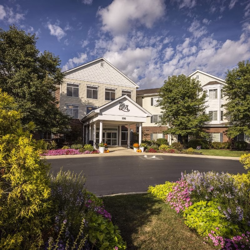 Mobile header view of Willow Brook Run in Delaware, Ohio, showing the welcoming covered entrance and lush gardens that greet visitors to this independent and assisted living community.