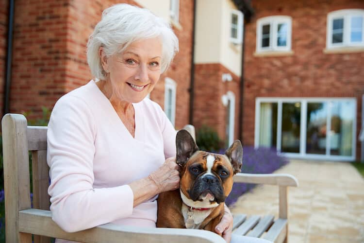A senior woman with her dog sitting outside an assisted living community.